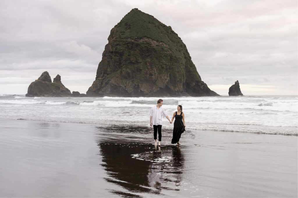 A photo of a couple walking on Cannon Beach in-front of Haystack Rock in Oregon. Photo taken by Kollar Photography. Arizona Elopement Photographer 