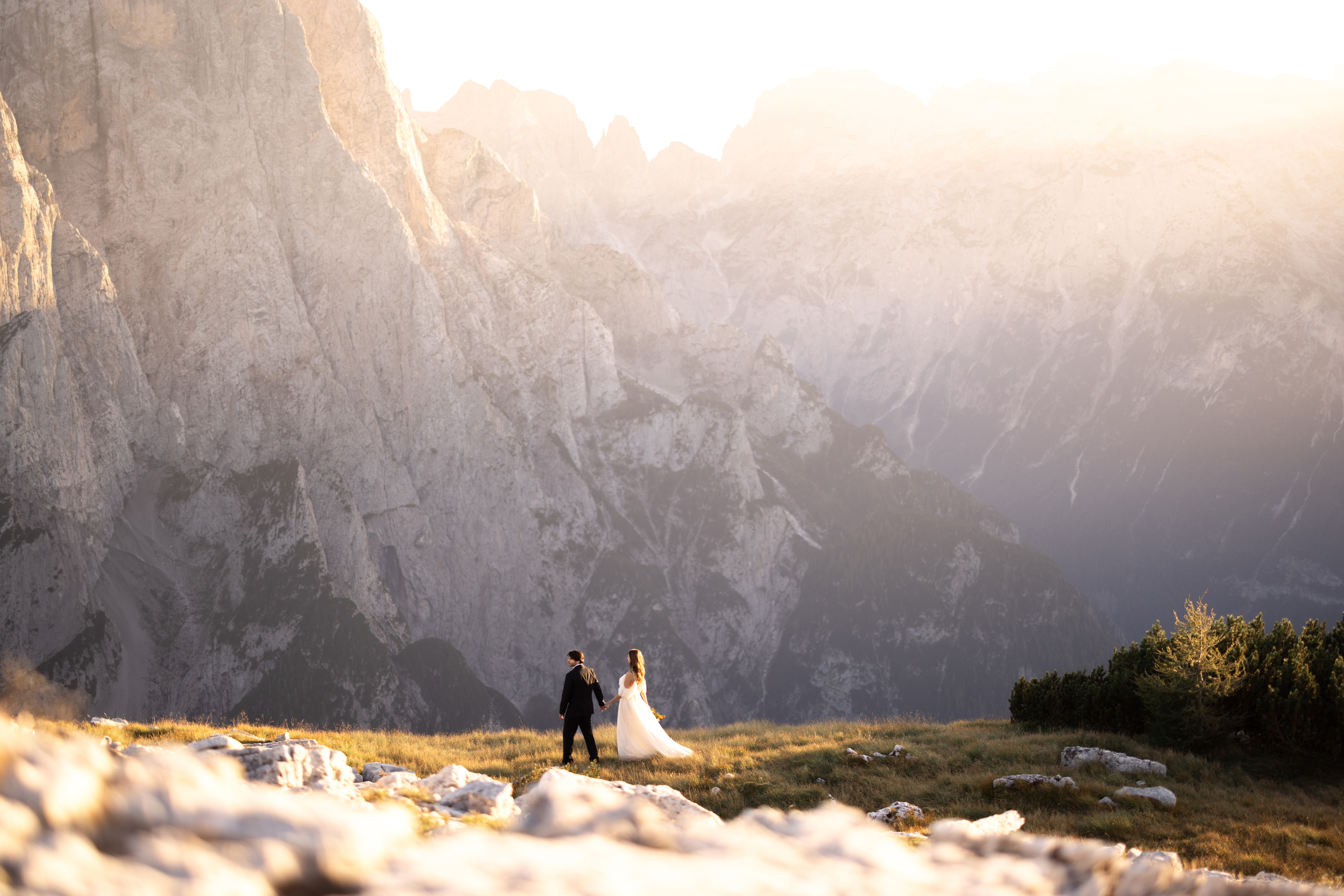 A romantic couple standing on a scenic mountain peak with golden light illuminating the rugged landscape, perfect for a destination wedding moment.