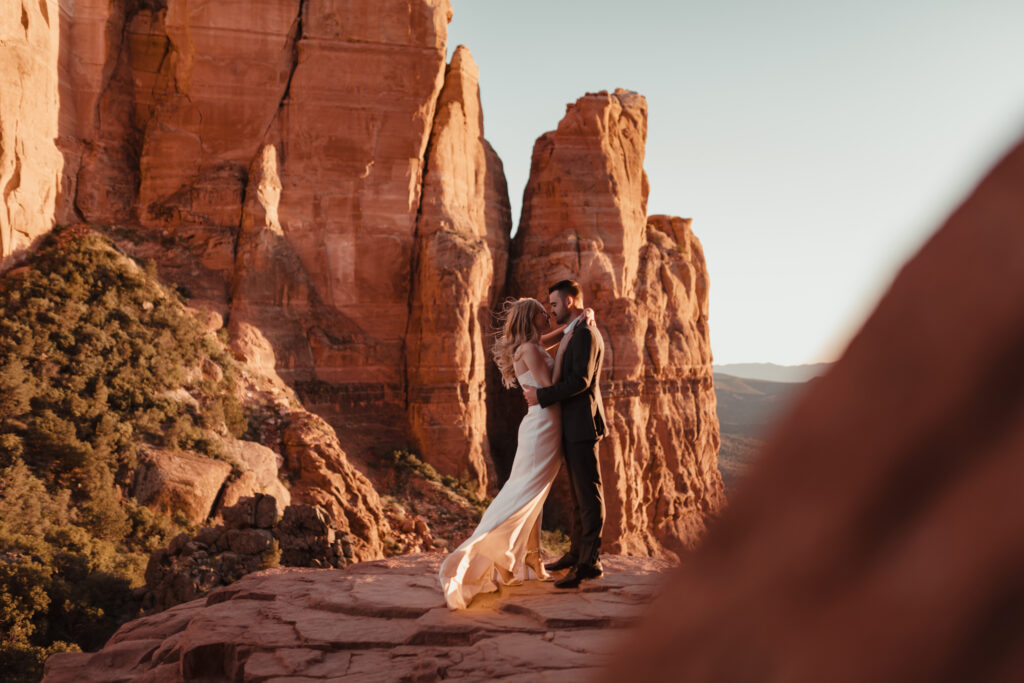 Bride in a flowy bohemian wedding dress standing on a red rock ledge in Sedona, Arizona.