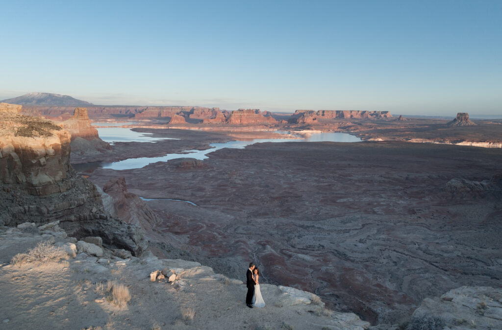 A dreamy elopement moment on a secluded Lake Powell beach, with the couple barefoot in the sand and sandstone cliffs rising behind them.